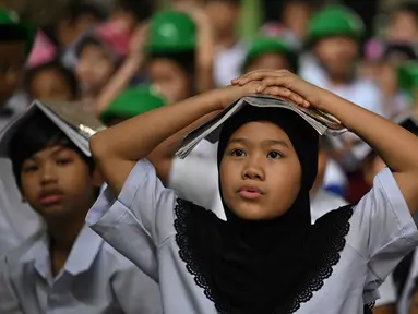 Para pelajar muda meletakkan buku di kepala mereka saat berkumpul di pusat evakuasi yang telah ditentukan di luar gedung sekolah selama latihan gempa bumi di salah satu sekolah dasar di Manila, Filipina pada 11 September 2025. (Ted ALJIBE/AFP)