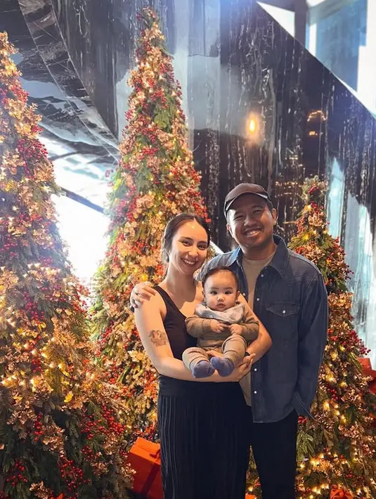 Joshua Suherman dan istri serta anaknya pun berfoto di depan pohon natal. Joshua tampil dengan kemeja denim dan istrinya dengan atasan tanktop serta rok pleated hitam. [@jojosuherman]
