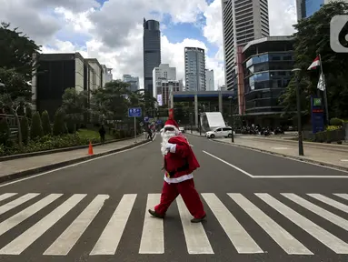 Pria berkostum Sinterklas menyeberang jalan saat membagikan kopi gratis kepada warga di kawasan Jalan Jenderal Sudirman, Jakarta, Sabtu (19/12/2020). Pembagian kopi tersebut bertujuan untuk menyambut perayaan Natal 2020. (Liputan6.com/Johan Tallo)