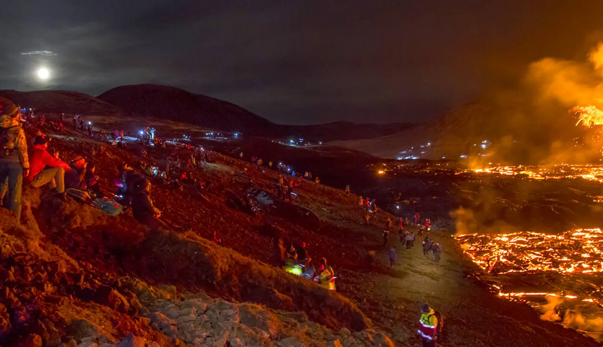 Orang-orang menyaksikan aliran lahar dari letusan gunung berapi di Semenanjung Reykjanes, barat daya Islandia, Senin (29/3/2021). Letusan gunung berapi tersebut tidak dipandang sebagai ancaman bagi kota-kota sekitar dan warga yang menyaksikan dari dekat. (AP Photo/Marco Di Marco)