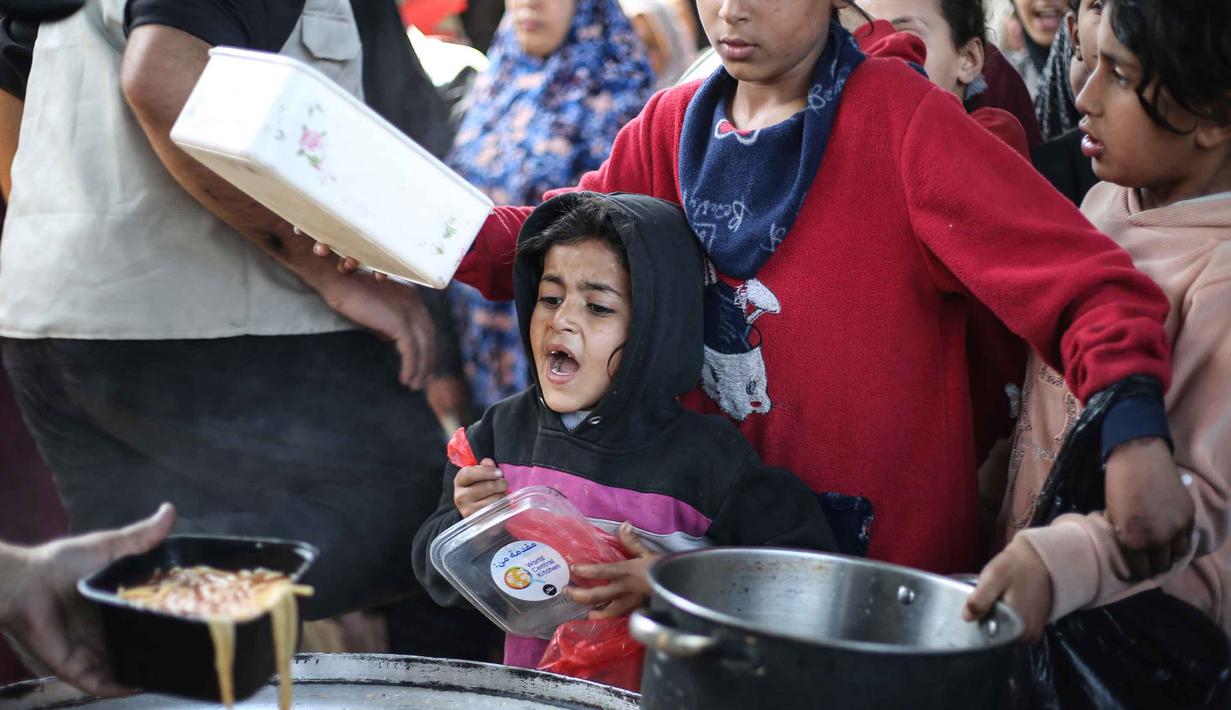 Kantor media pemerintah Gaza dalam pernyataannya pada Minggu 12 April 2026, menyebut kondisi saat ini sebagai dampak pembatasan pasokan yang terus berlangsung oleh Israel. Tampak dalam foto, anak-anak pengungsi Palestina menerima makanan dari dapur amal di kamp pengungsi Nuseirat, Jalur Gaza Tengah pada 13 April 2026. (Eyad Baba/AFP)