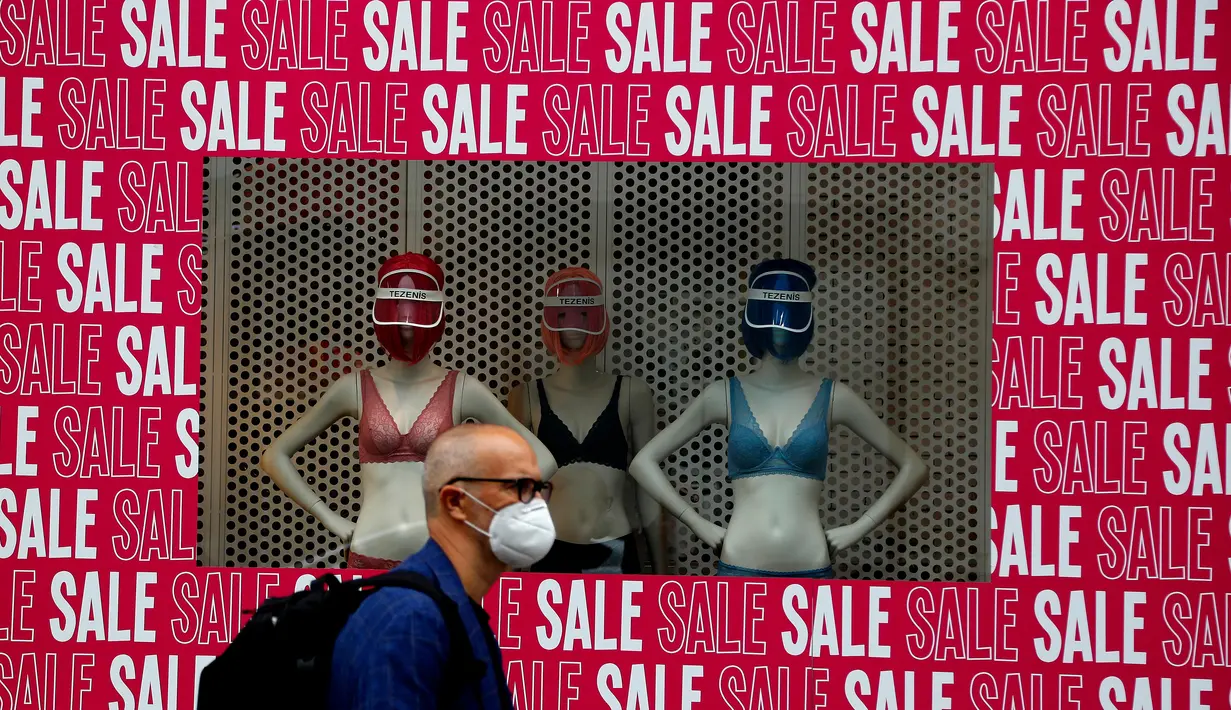 Seorang pria mengenakan masker berjalan melewati jendela toko di London, Selasa (14/7/2020). Pemerintah Inggris menuntut warga mengenakan masker di toko-toko di tengah pandemi COVID-19. (AP Photo/Frank Augstein)