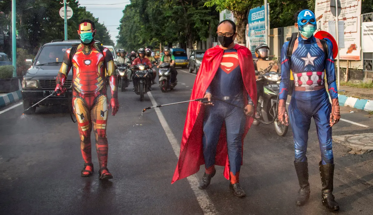 Petugas kepolisian yang berpakaian superhero menyemprotkan cairan disinfektan di jalan kawasan Pasuruan, Jawa Timur, Kamis (9/4/2020). Penyemprotan cairan disinfektan tersebut bertujuan untuk mengantisipasi penyebaran Virus Corona (COVID-19). (JUNI KRISWANTO / AFP)