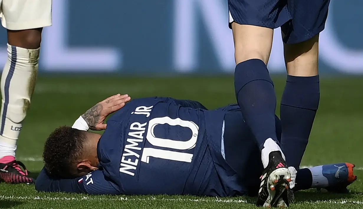 Pemain Paris Saint-Germain (PSG), Neymar, terbaring saat cedera setelah berebut bola dengan pemain Lille, Benjamin Andre, pada laga Liga Prancis di Stadion Parc des Princes, Minggu (19/2/2023). Neymar pun terpaksa ditarik keluar lapangan sembari menangis karena kesakitan. (AFP/Frank Fife)