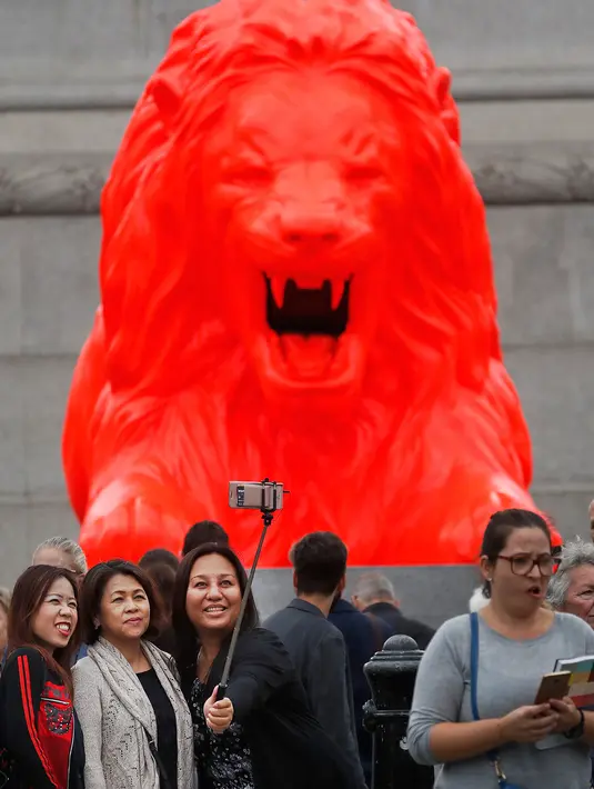 Sejumlah wanita berselfie di depan singa fluorescent merah di pangkalan Kolom Nelson di Trafalgar Square di London (19/9). Singa merah baru merupakan proyek seni yang diciptakan oleh perancang Es Devlin. (AP Photo/Frank Augstein)