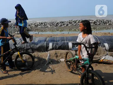 Anak-anak bermain sepeda di atas tumpukan karung pasir yang menjadi penahan datangnya gelomba dan abrasi di pesisir pantai Pisangan, Desa Cemara Jaya, Kecamatan Cibuaya, Kabupaten Karawang, Jawa Barat, Sabtu (27/5/2023). (merdeka.com/Imam Buhori)