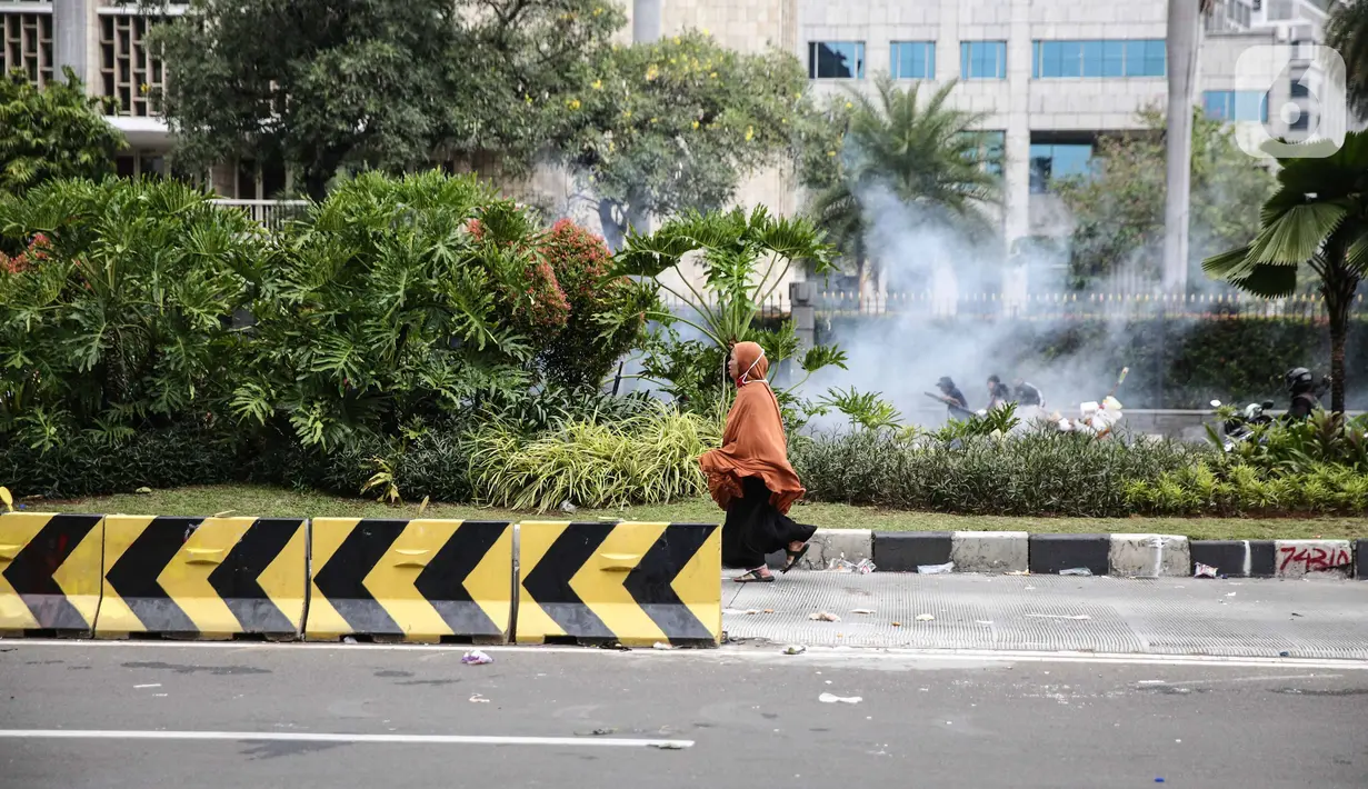 Seorang perempuan berlari di tengah massa pendemo yang terlibat bentrok dengan polisi di kawasan Patung Kuda, Jakarta, Selasa (13/10/2020). Perempuan yang terjebak itu diselamatkan pendemo saat unjuk rasa menolak Omnibus Law Undang-Undang Cipta Kerja tersebut ricuh. (Liputan6.com/Faizal Fanani)