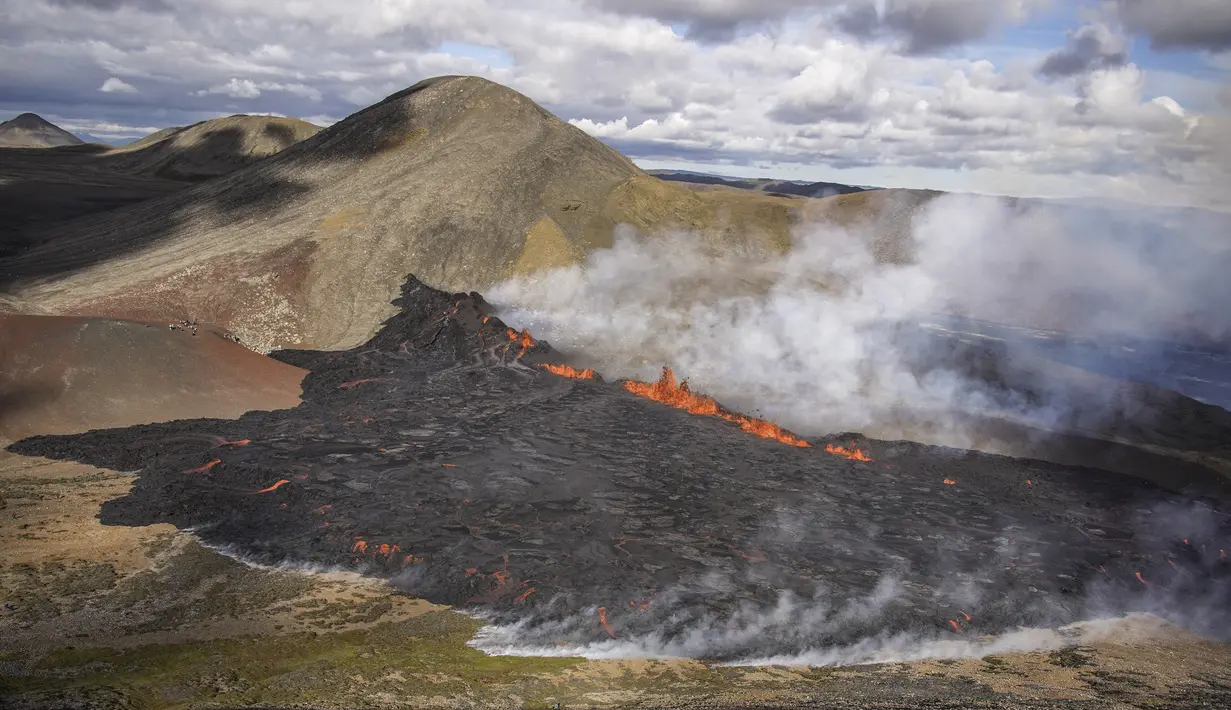 Uap naik dan lava mengalir dari gunung berapi Fagradalsfjall di Islandia pada Rabu (3/8/2022), yang terletak 32 kilometer (20 mil) barat daya ibu kota Reykjavik dan dekat dengan Bandara Internasional Keflavik. Kode merah diumumkan  untuk melarang pesawat terbang di atas lokasi langsung meskipun helikopter akan dikirim untuk mengamati situasi. (AP Photo/Marco Di Marco)