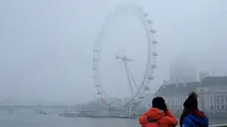 Wisatawan mengambil gambar The London Eye saat diselimuti kabut Inggris, Senin, (23/1). Aktifitas warga menjadi terganggu karena terbatasnya jarak pandang (AP Photo / Alastair Grant)