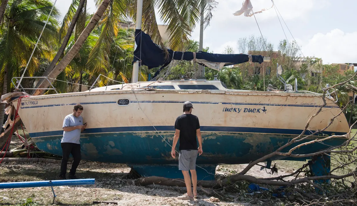 Dua orang pria berdiri dekat sebuah kapal yang terhempas ke daratan akibat terhempas badai Irma di Coconut Grove, Florida, Senin (11/9).Badai Irma menghantam negara bagian Florida dengan kecepatan angin mencapai 200 km/jam. (SAUL LOEB/AFP)