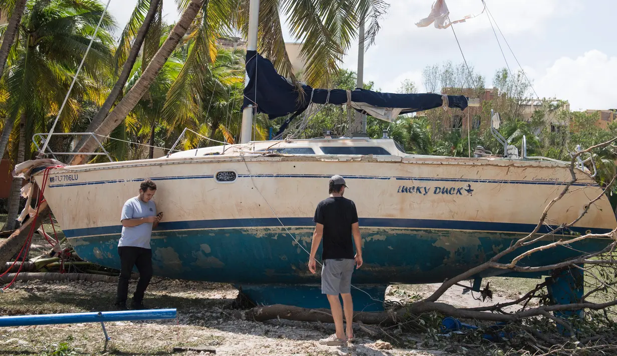 Dua orang pria berdiri dekat sebuah kapal yang terhempas ke daratan akibat terhempas badai Irma di Coconut Grove, Florida, Senin (11/9).Badai Irma menghantam negara bagian Florida dengan kecepatan angin mencapai 200 km/jam. (SAUL LOEB/AFP)