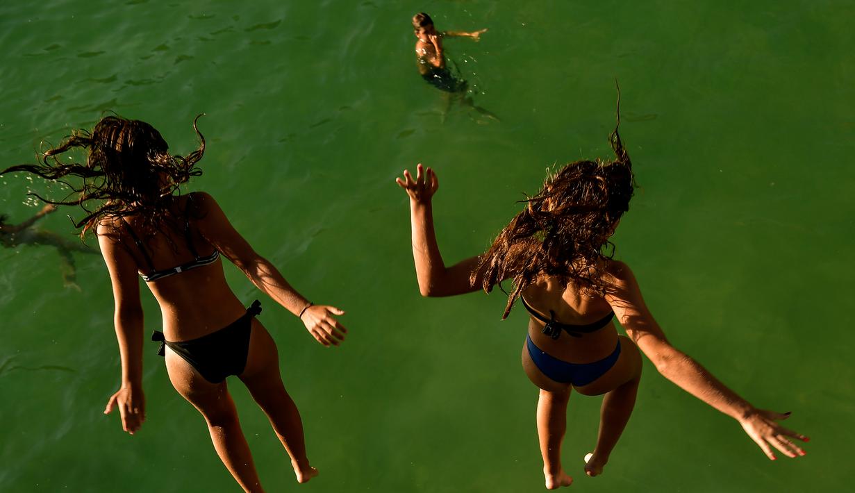 Dua wanita melompat ke air di pantai La Concha saat musim panas di kota basque San Sebastian, Spanyol (3/8).  Udara panas dari Afrika membawa gelombang panas ke Eropa, mendorong peringatan kesehatan tentang debu Sahara Desert. (AP Photo/Alvaro Barrientos)