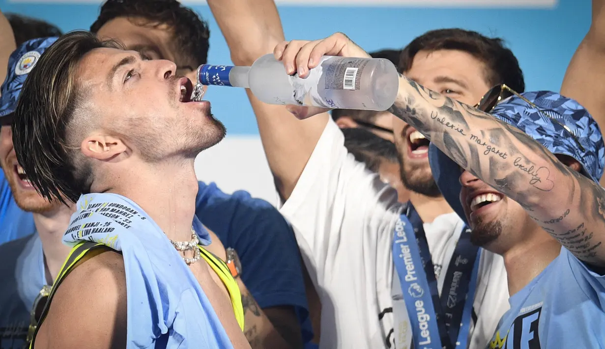 Pemain Manchester City, Jack Grealish (kiri), menikmati minuman beralkohol yang diberikan rekan satu timnya, Kalvin Phillips (kanan) dalam perayaan Trebele Winners di kota Manchester, Selasa (13/6/2023) dini hari WIB. (AFP/Oli Scarff)