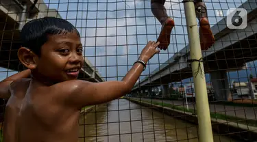 Anak-anak bermain dan berenang di aliran Kalimalang, Jakarta, Sabtu (15/2/2020). Cuaca yang tidak menentu membuat aliran air terkadang menjadi deras sehingga akan membahayakan keselamatan anak-anak saat bermain dan berenang. (merdeka.com/Imam Buhori)