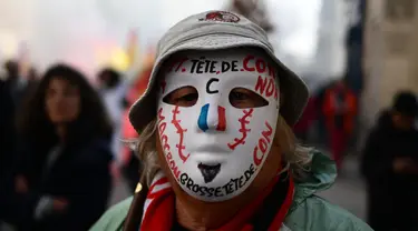 Seorang pengunjuk rasa mengenakan topeng bertuliskan slogan-slogan selama demonstrasi pada hari kelima demonstrasi nasional yang diselenggarakan sejak awal tahun, menentang perombakan pensiun yang sangat tidak populer, di Avignon, Prancis Selatan, Kamis (16/2/2023). (CHRISTOPHE SIMON/AFP)