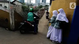 Pengendara sepeda motor melintasi jalur alternatif saat anak sekolah berjalan di belakang Kompleks Patra Jasa, Jakarta Selatan, Rabu (1/3/2023). Jalur alternatif seperti gang, jalan kecil, maupun jalan tembusan menjadi pilihan bagi pengendara sepeda motor untuk menghindari kemacetan di jalan-jalan protokol Ibu Kota. (Liputan6.com/Johan Tallo)