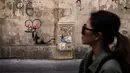 Seorang wanita berjalan melewati mural yang diduga karya seniman sekaligus aktivis Banksy di Paris, Prancis, Minggu (24/6). Karya seni ini muncul bertepatan dengan Hari Pengungsi Dunia. (PHILIPPE LOPEZ/AFP)