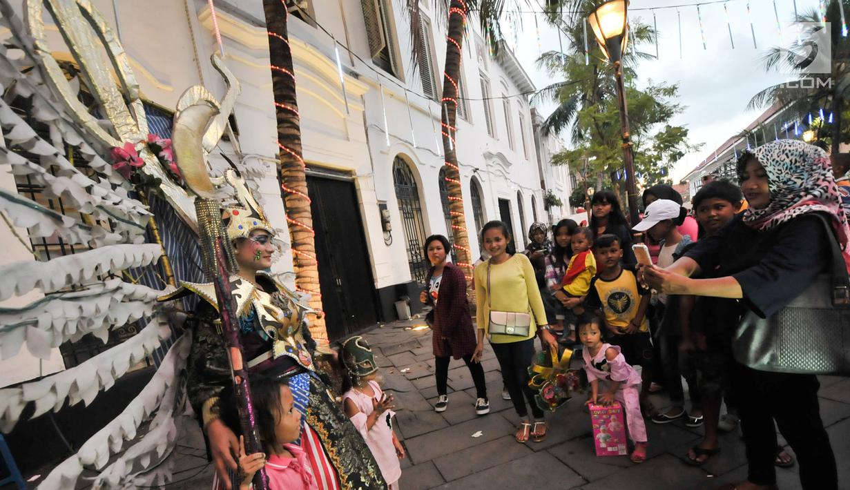Pengunjung berfoto dengan wanita yang mengenakan kostum di kawasan wisata Kota Tua, Jakarta, Selasa (27/6). Memasuki libur lebaran hari ke-3, kawasan wisata Kota Tua penuh dikunjungi warga. (Liputan6.com/Yoppy Renato)