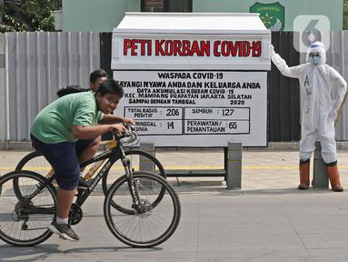 Pesepeda melintas di depan seni instalasi yang menggambarkan tenaga medis memegang peti jenazah korban COVID-19 di Kemang 1, Jakarta Selatan, Minggu (16/8/2020). Seni instalasi itu dipajang guna memberi peringatan kepada warga untuk tetap waspada terhadap COVID-19. (Liputan6.com/Herman Zakharia)