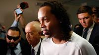 Mantan pemain timnas Brasil, Ronaldinho dikawal oleh polisi meninggalkan kantor pengadilan di Asuncion, ibu kota Paraguay, Jumat (6/3/2020). Ronaldinho bersama saudara laki-lakinya berurusan dengan pihak berwenang Paraguay karena menggunakan paspor palsu untuk memasuki negara itu. (AP/Jorge Saenz)