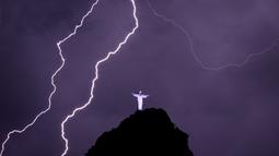 Petir menyambar di dekat patung Kristus Penebus di gunung Corcovado di Rio de Janeiro, Brasil, Selasa (21/2/2023). Pada 2007, Patung Yesus Kristus ini masuk dalam tujuh keajaiban dunia.  (Photo by MAURO PIMENTEL / AFP)