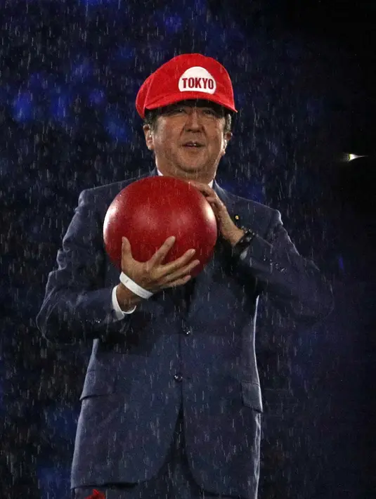 Penampilan PM Jepang, Shinzo Abe ketika mengenakan topi khas Mario Bros pada upacara penutupan Olimpiade Rio 2016 di Rio de Janeiro, Minggu (21/8). Shinzo Abe sempat menyamar menjadi Mario Bros untuk mempromosikan Olimpiade Tokyo 2020. (Stoyan Nenov/AFP)
