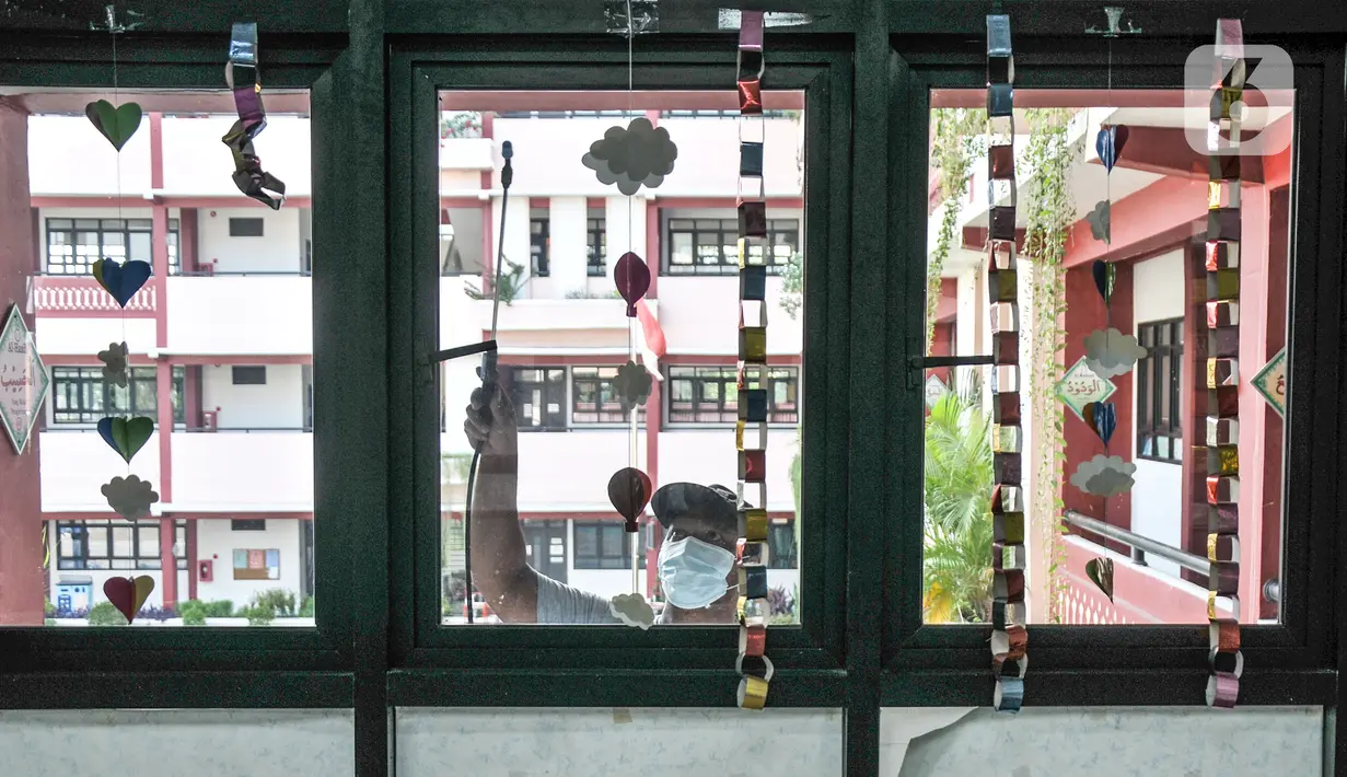 Petugas menyemprotkan disinfektan pada kaca ruang kelas di SD Negeri Malaka Jaya 07 Pagi, Jakarta, Kamis (26/8/2021). Pemprov DKI berencana membuka kembali sekolah untuk pembelajaran tatap muka terbatas pada Senin (30/8) setelah status PPKM turun ke level 3. (merdeka.com/Iqbal S Nugroho)