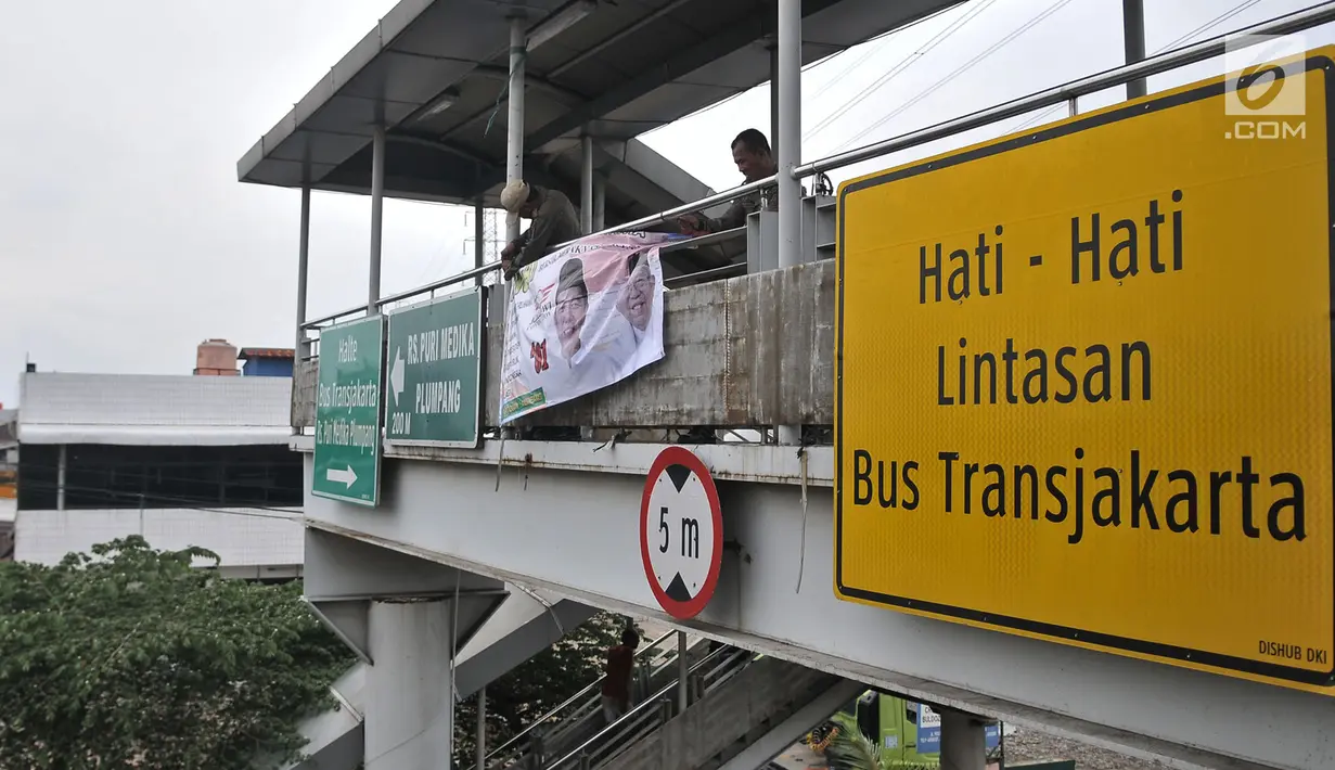 Petugas Satpol PP mencopot spanduk APK yang terpasang di JPO di sepanjang Jalan Yos Sudarso, Jakarta, Rabu (13/3). Bawaslu menginstruksikan Pemkot se-DKI Jakarta untuk menertibkan APK yang dipasang di sembarang tempat. (merdeka.com/Iqbal S. Nugroho)