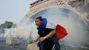 Seorang demonstran berlari menghindari gas air mata yang ditembakan polisi di bawah Menara Eiffel di dekat zona penggemar Paris sebelum laga Portugal vs Prancis di Final EURO 2016 di Prancis (10/6). (REUTERS/Stephane Mahe)