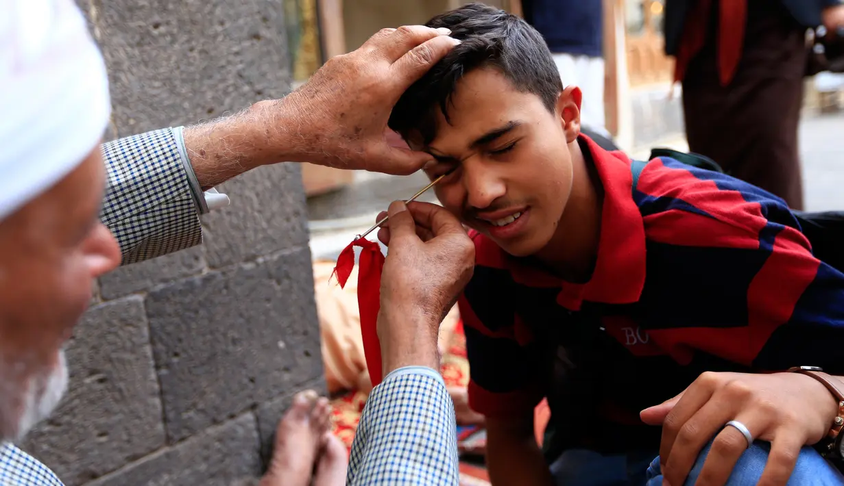 Seorang pria Yaman mengoleskan kosmetik tradisional kohl ke kelopak mata pria lain di Masjid Agung, kota tua Sanaa pada 9 mei 2019. Bagi muslim Yaman, pemakaian kohl diyakini mampu membersihkan dan melindungi mata dari penyakit ini sudah menjadi tradisi setiap bulan Ramadan. (MOHAMMED HUWAIS/AFP)