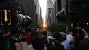 Orang-orang mengambil gambar saat matahari terbenam di Manhattan ketika fenomena "Manhattanhenge" di 42nd street, New York, Senin (11/7/2022). Fenomena Manhattanhenge hanyaterjadi di musim panas, tepatnya diantara bulan Mei hingga Juli. (Yuki IWAMURA / AFP)