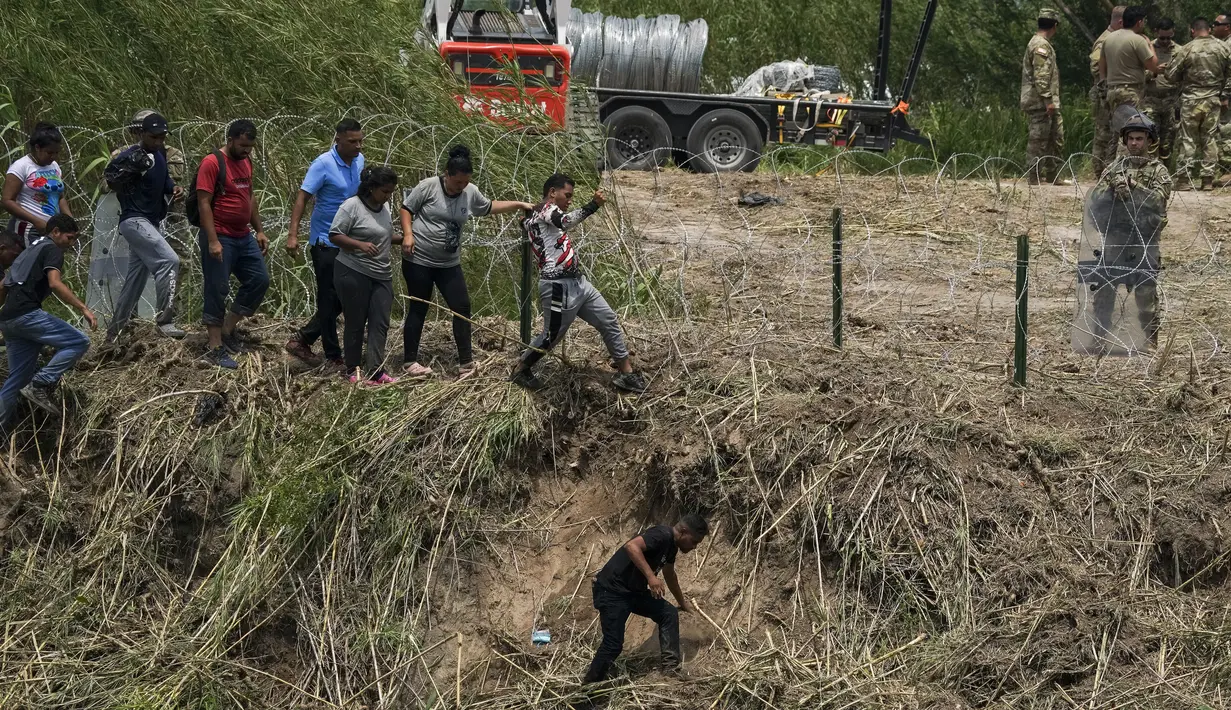Di sisi sungai AS, para migran mengenakan pakaian kering dan melewati kawat berduri. (AP Photo/Fernando Llano)