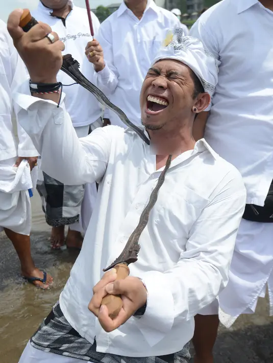 Seorang pria menusukkan keris ke lehernya saat menggelar ritual Melasti di Pantai Petitenget, Denpasar, Bali, Senin (4/3). Tidak sedikit warga yang kesurupan saat mengikuti upacara ini. (SONNY TUMBELAKA/AFP)
