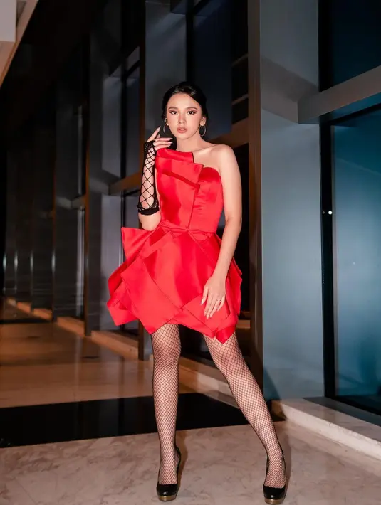 Tampil dengan siluet yang lebih berani, Lyodra mengenakan off-the-shoulder mini dress berwarna merah. Dress yang dirancang dengan kesan tumpuk ini kemudian disempurnakan dengan stoking jaring-jaring, dan glove jaring yang dikenakan di sebelah tangan saja. Foto: Instagram.