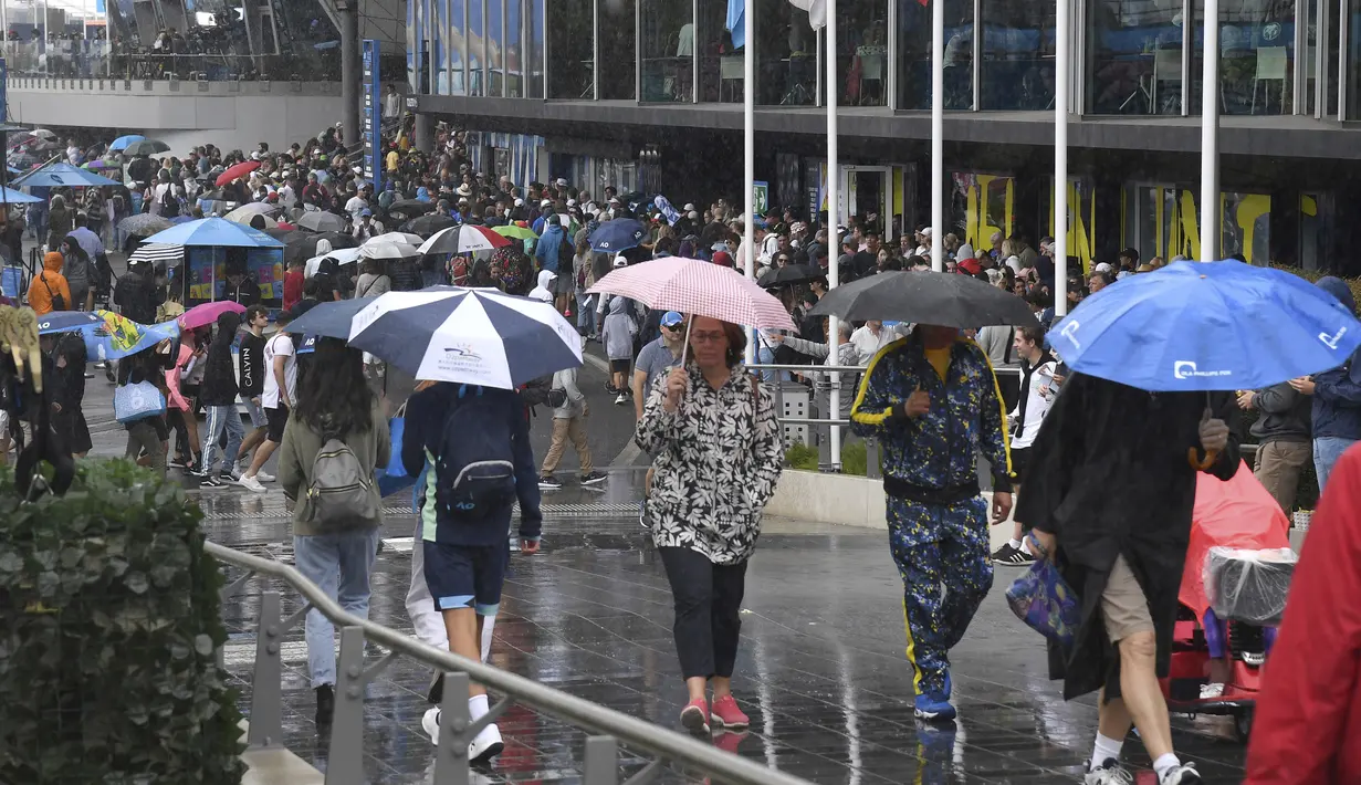 Penonton berjalan di tengah hujan saat permainan dihentikan don the court luar saat pertandingan tunggal putaran pertama mereka di kejuaraan tenis Australia Terbuka di Melbourne, Australia, Senin (20/1/2020). (AP Photo/Andy Brownbill)