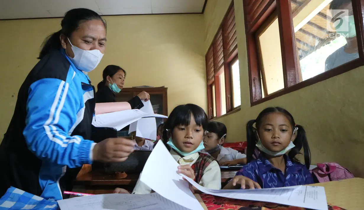 Guru membagikan soal UAS ke siswa SDN 4 Rendang di Karangasem, Bali, Rabu (29/11). Kegiatan di beberapa sekolah yang masuk dalam kawasan KRB Gunung Agung masih terlihat meski beberapa wilayah di Karangasem mengalami hujan abu (Liputan6.com/Andi Jatmiko)