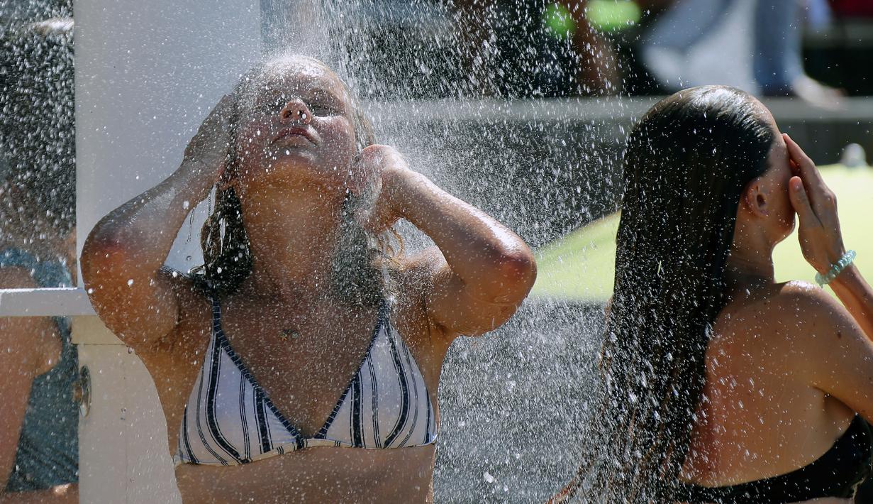 Dua wanita mendinginkan diri di bawah pancuran di pantai Biarritz, barat daya Prancis, (3/8). Cuaca panas diperkirakan akan berlangsung selama beberapa hari di eropa. (AP Photo/Bob Edme)