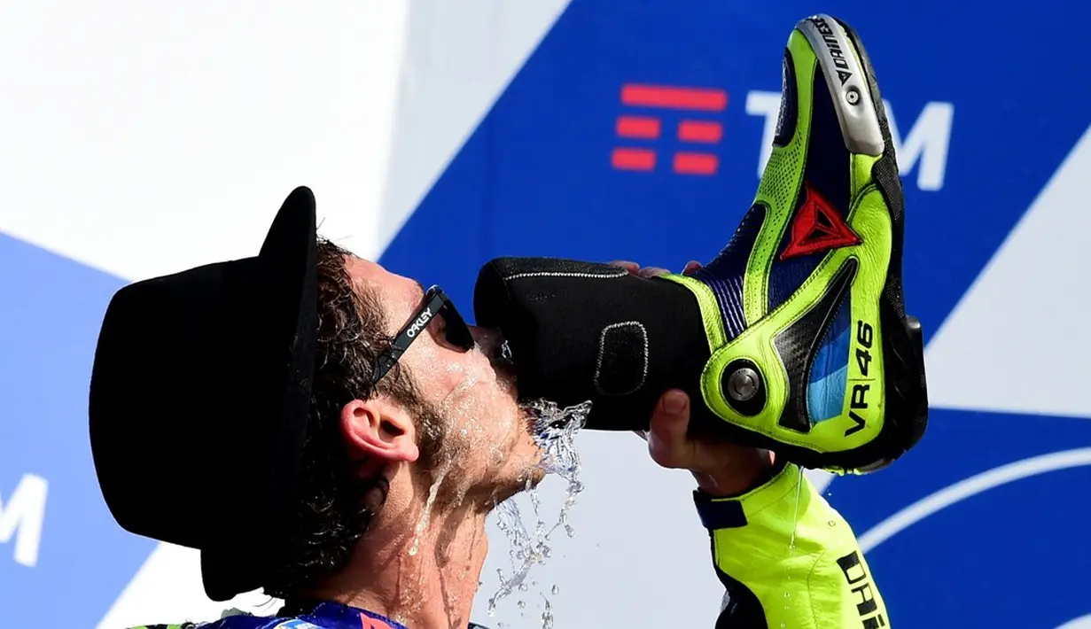 Valentino Rossi merayakan kemenangan dengan minum sampanye dari sepatunya saat berada di podium MotoGP San Marino di Sirkuit Misano, Minggu (11/9/2016). (AFP/Giuseppe Cacace))
