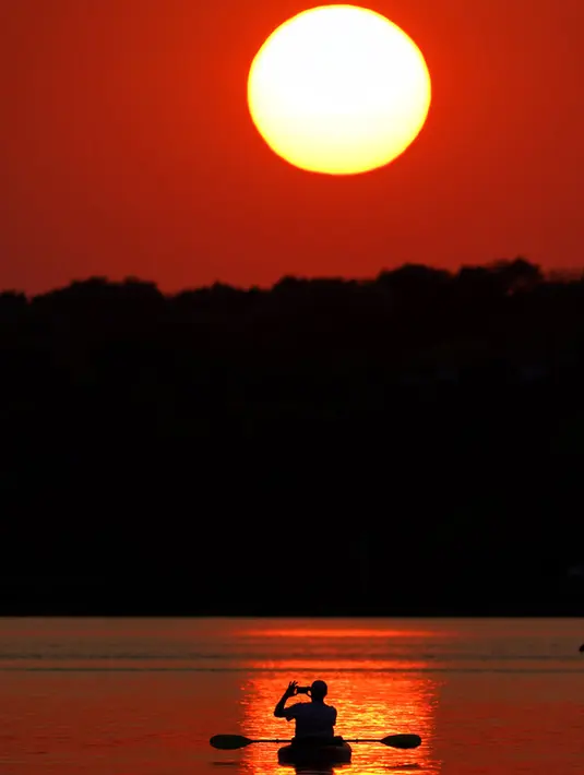 Seorang pria memotret matahari terbenam saat berperahu di Shawnee Mission Lake, Shawnee, Kansas, Amerika Serikat, Jumat (9/10/2020). Matahari terbenam terus lebih cerah dari biasanya karena asap dari kebakaran hutan barat terus melayang di seluruh negeri. (AP Photo/Charlie Riedel)