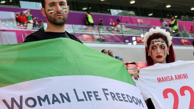 An Iran supporter with blood tears makeup on her face holds a jersey with the name of Mahsa Amini with another supporter holding a flag reading "Woman life freedom" as they attend the match between Wales and Iran.