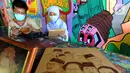 Arfan (55) seniman pelukis bakar atau pyrography bersama istri menyelesaikan karya seni lukis bakar di atas media kayu dan kulit  di galeri Rumah Oenik, Kampung Ragamukti, Tajur Halang, Bogor, Senin (28/9/2020). (Merdeka.com/Arie Basuki)