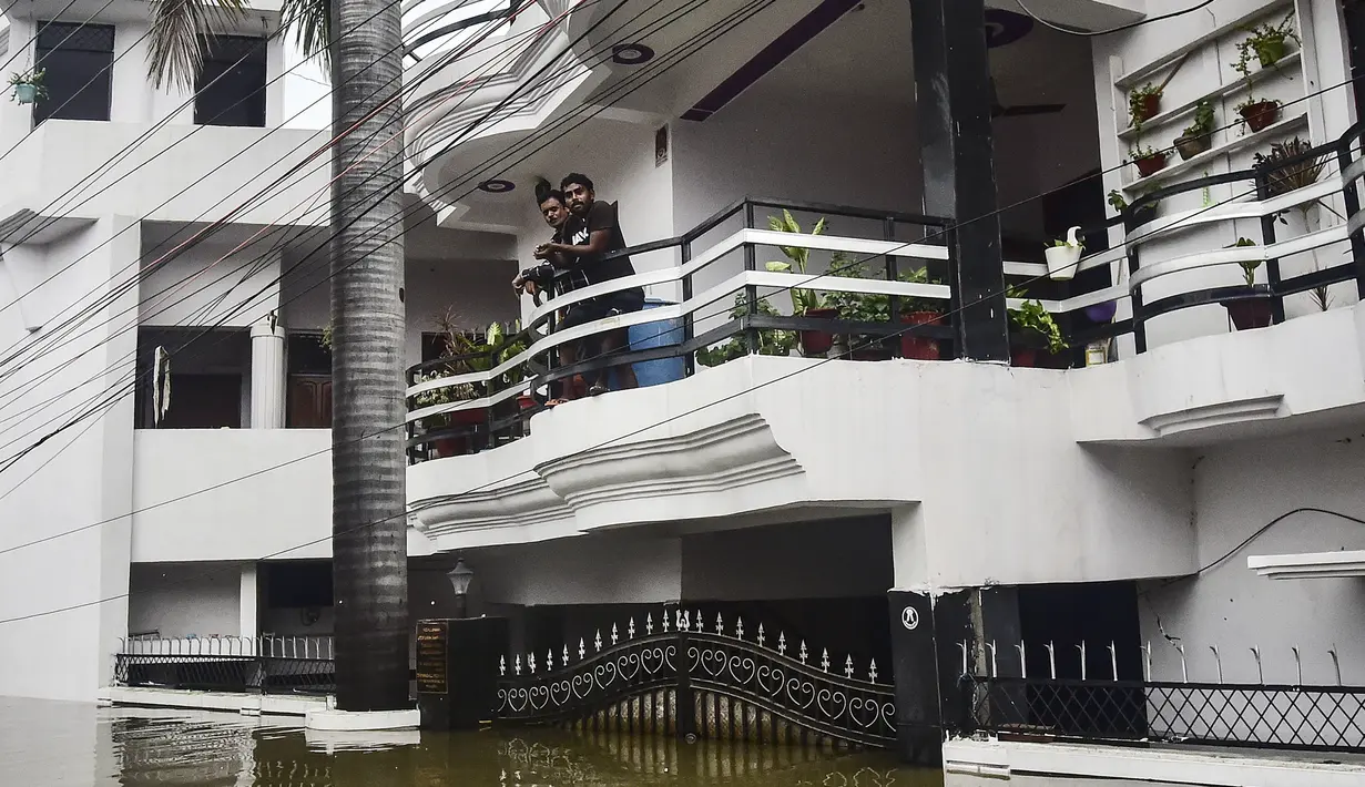 Warga melihat keluar dari balkon saat banjir di Chhota Baghara, Allahabad, India, Rabu (11/8/2021). Hujan lebat menyebabkan banjir di Allahabad. (SANJAY KANOJIA/AFP)