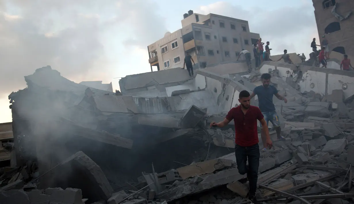 Sejumlah pria berjalan di puing-puing bangunan yang hancur akibat serangan udara Israel di Kota Gaza, Palestina, (9/8). Kementerian Kesehatan Palestina mengatakan beberapa pengamat terluka dalam serangan di Kamp pengungsi Shati. (AP Photo/Khalil Hamra)