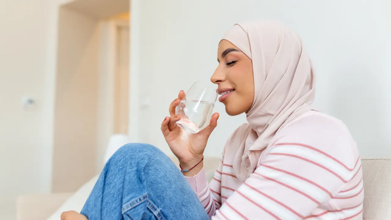 Seorang wanita muslimah mengenakan jilbab pink sedang minum air putih (Foto Dok: Freepik/ stefamerpik)