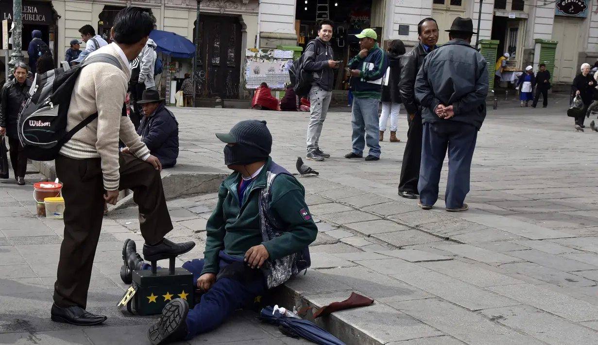Tukang semir sepatu bertopeng melayani pelanggannya di kawasan La Paz, Bolivia (29/11). Dengan menutup wajahnya para tukang semir ini menyembunyikan identitas karena pekerjaan tersebut dipandang rendah oleh masyarakat lokal. (AFP PHOTO/Aizar Raldes)
