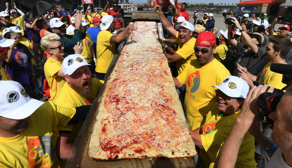 Peserta menunjukan pizza yang telah selesai dibuat di jalur Auto Club Speedway, di Fontana, California (10/6). Mereka berhasil memecahkan rekor Guinness World Records untuk pizza terpanjang di dunia dengan panjang 1,32 mil atau 2,13 km. (AFP/Mark Ralston)