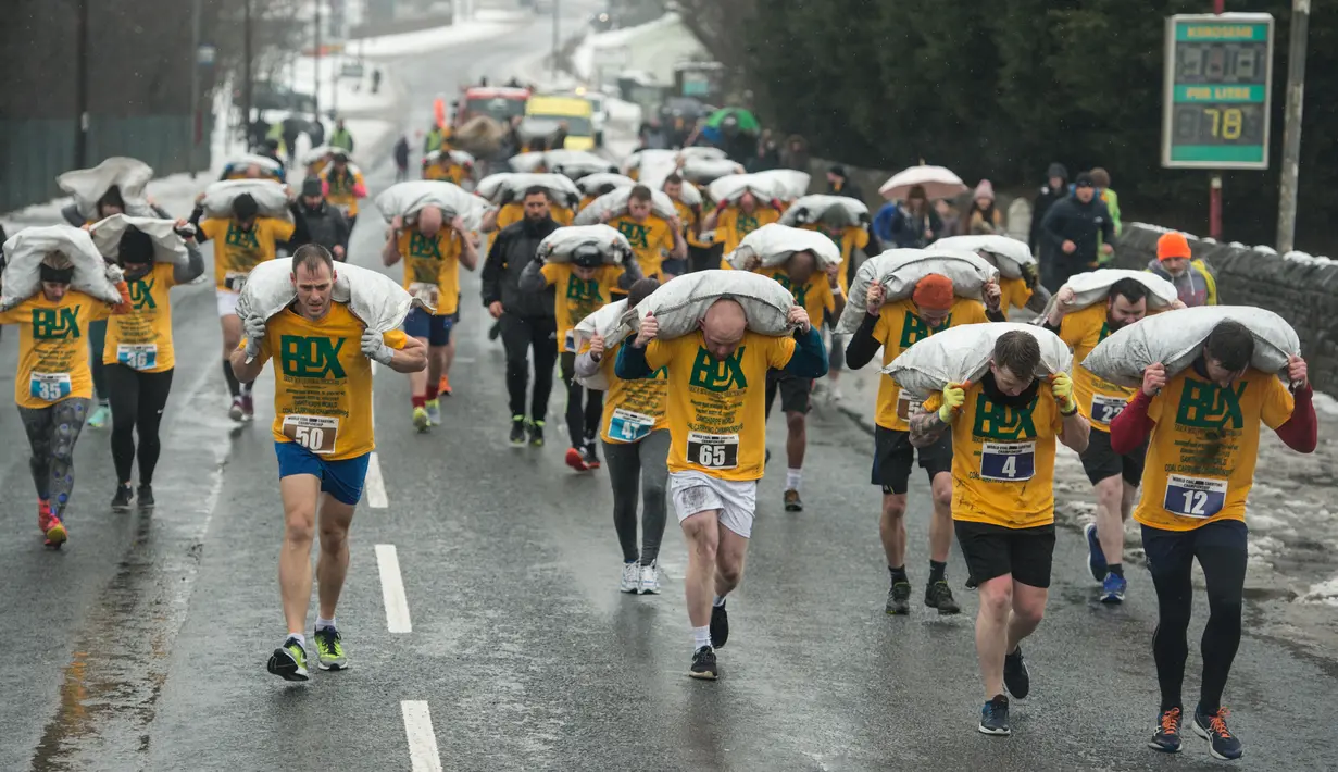 Peserta membawa karung berisi batu bara saat mengikuti World Coal Carrying Championships di Desa Gawthorpe, Wakefield, Inggris Utara, Senin (2/4). Kompetisi  tahunan mengakut karung batu bara ini dalam memperingati Senin Paskah. (OLI SCARFF/AFP)