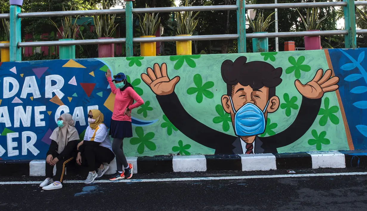 Warga berpose dengan mural yang mengajak orang untuk memakai masker di tengah pandemi Covid-19 di Surabaya, Jawa Timur, Minggu (25/10/2020). Mural di sepanjang dinding itu sebagai sarana imbauan kepada masyarakat untuk menerapkan protokol kesehatan pencegahan penularan COVID-19. (Juni Kriswanto/AFP)