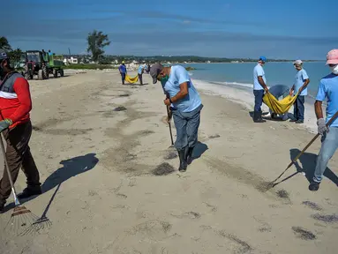 Para pekerja dengan mengenakan masker membersihkan pantai di Havana pada Senin (15/6/2020). Kuba akan menguji semua pelancong untuk Covid-19 dan membatasi kontak mereka dengan penduduk setempat ketika perbatasan dibuka kembali untuk turis asing. (Yamil LAGE / AFP)
