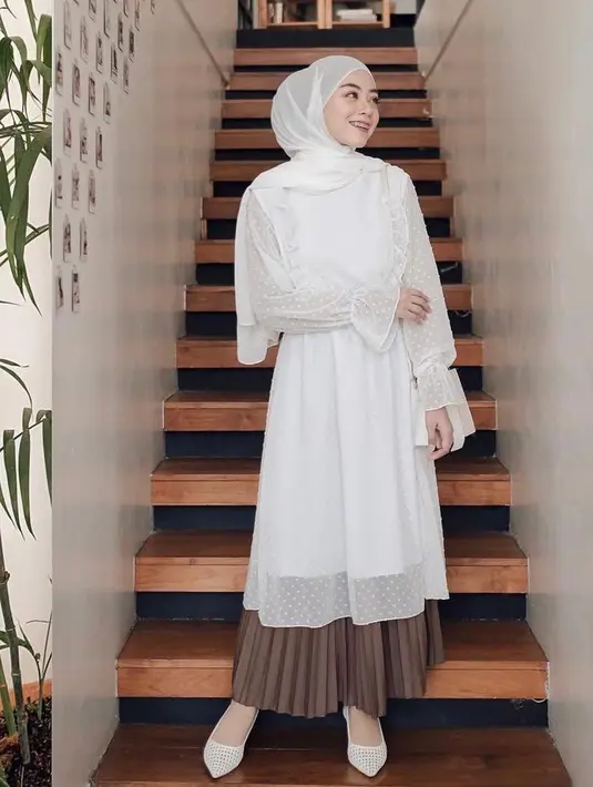 <p>Look feminin berikut ini cocok untuk busana ke kondangan, padukan tunik warna putih dengan rok plisket warna cokelat. (Instagram/meiraniap).</p>